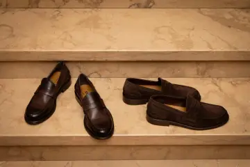 Due paia di mocassini uomo marroni, uno in pelle lucida e l'altro in camoscio, perfetti per un outfit elegante.