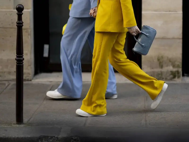 Un outfit tailleur con sneakers, giallo brillante e azzurro polvere, camminano sul marciapiede.